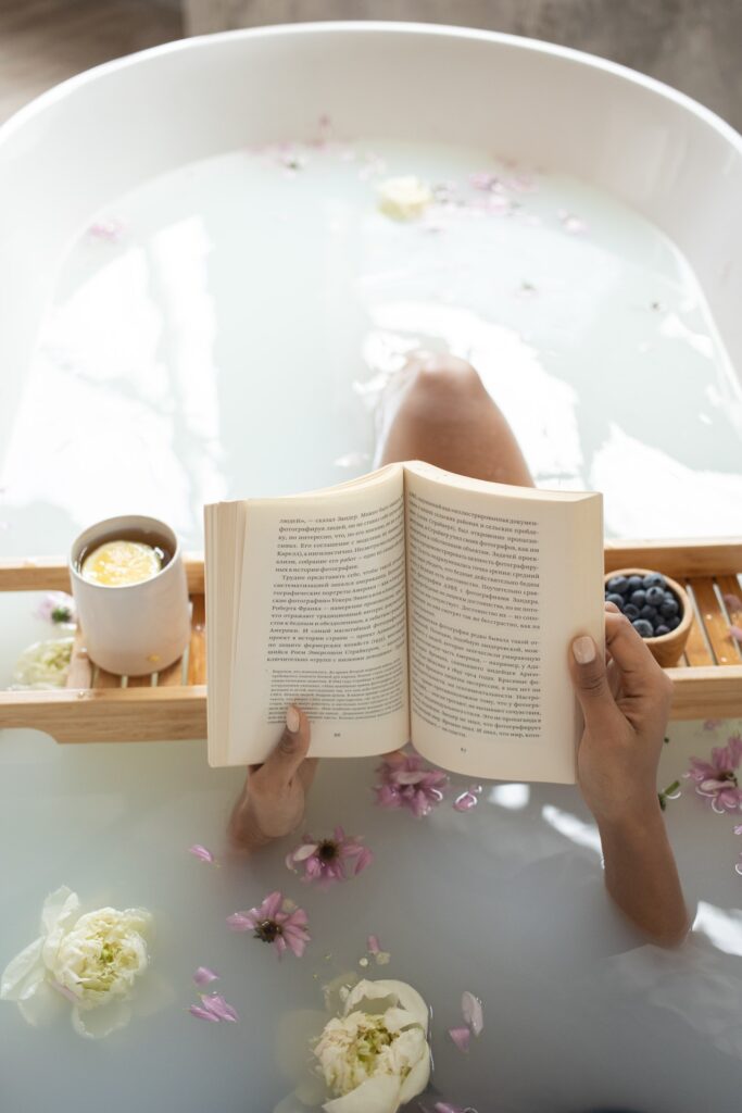 A serene retreat moment: person relaxing in a milk bath with a book, accompanied by tea and blueberries.